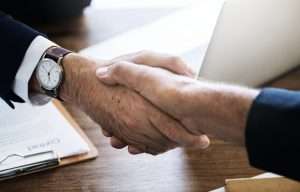 Aperto de mãos entre dois homens de terno, simbolizando um acordo comercial ou contrato. Imagem ideal para ilustrar negociações e estratégias para vender ao governo.