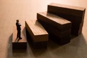 Homem em miniatura de terno observa escada de blocos de madeira, simbolizando o caminho estratégico de como ganhar licitação.