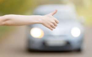 Mão estendida pedindo carona em estrada com carro se aproximando ao fundo, simbolizando oportunidade em licitação