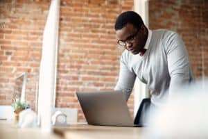 Empreendedor MEI analisando oportunidades de licitação pública no laptop em escritório moderno.
