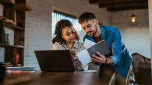 Pessoas conferindo informações em computador e documentos. Imagem ilustrativa para texto Como calcular preço inexequível em licitação.