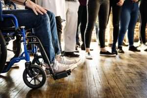 Pessoa em cadeira de rodas com colegas de trabalho ao lado, indicando as reservas de vagas para pessoas com deficiência
