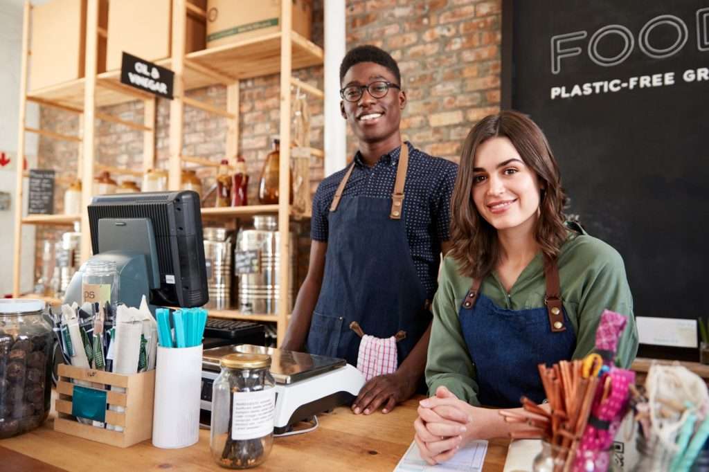 Dois atendentes sorridentes em uma loja sustentável, representando como o MEI pode participar de licitação e crescer no mercado público.