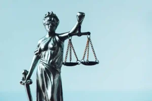 Estátua da Justiça em metal prateado segurando balança e espada, com foco nas correntes e nos pratos suspensos, evocando o debate sobre excesso de formalismo em licitação e a tensão entre rigor procedimental e eficiência nas contratações públicas eletrônicas.