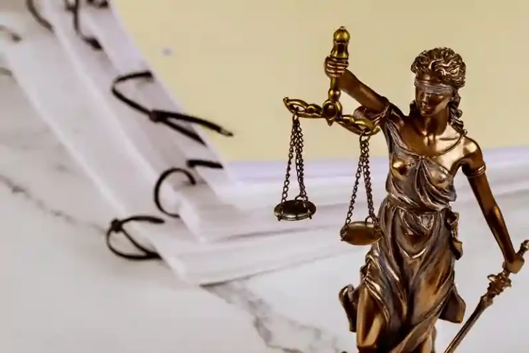 Estátua da Justiça com balança ao lado de documentos e óculos.